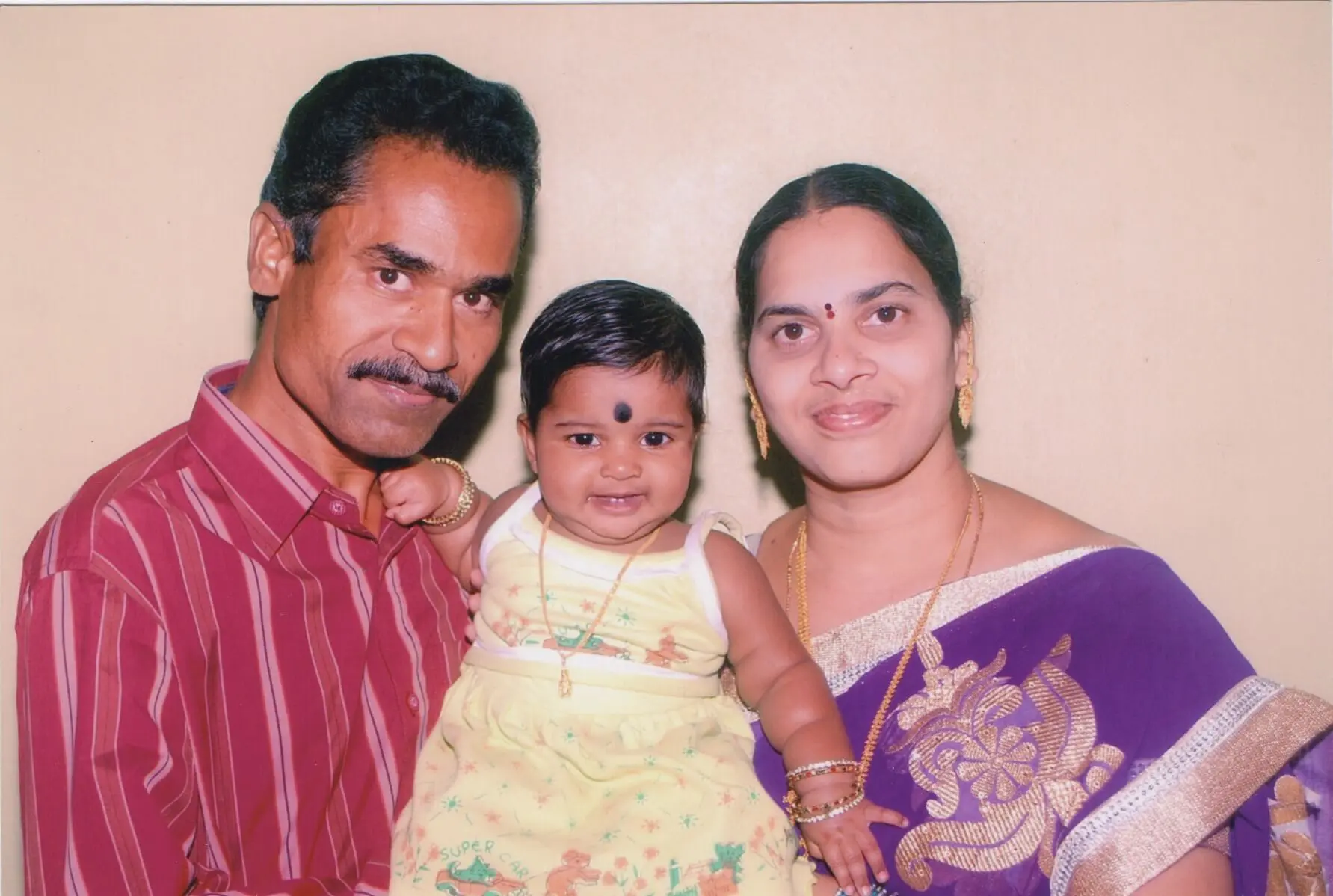 Child born by ICSI treatment at Karthika Datta's IVF clinic in 2012, seen smiling at the camera. Flanked by father (to the left) and mother to the right, both standing and holding the baby.