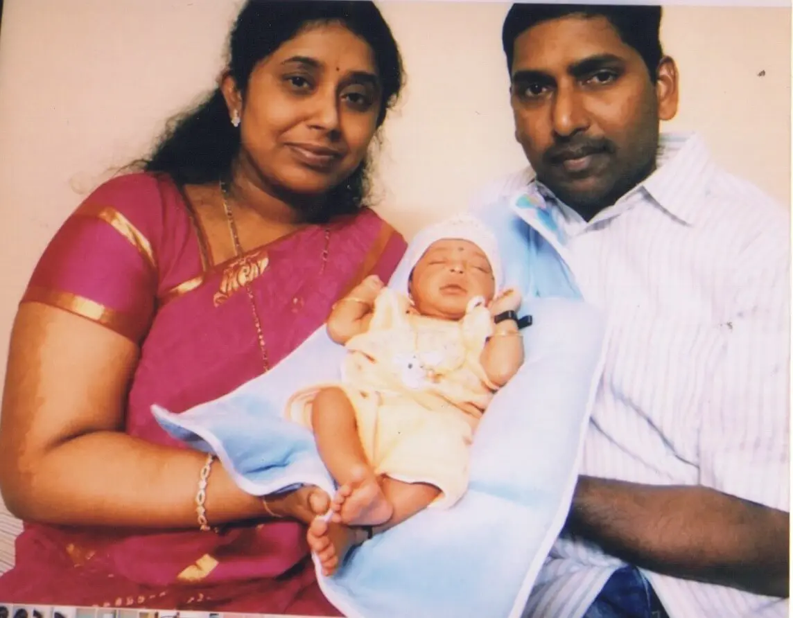 To the left, Mother holding a sleeping baby along with the father to the right. Baby born through ICSI at Karthika Datta's IVF. Photo from 2016.